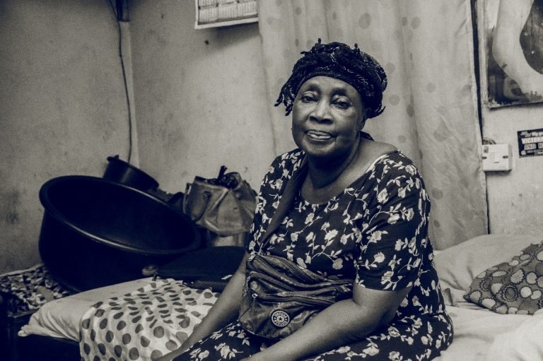 Asemota, sits on a bed in her single-room apartment.